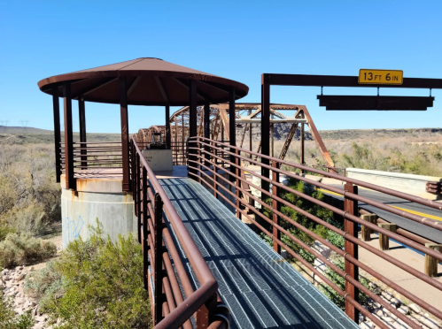 A metal walkway leads to a gazebo-like structure, with a height clearance sign above, surrounded by desert landscape.